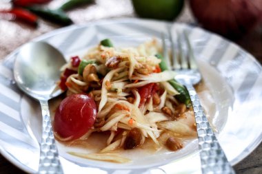 Tabakta Tayland papaya salatası, kakalı papaya salatası, limon, biber, ahşap masada beyaz kasede kırmızı domates.