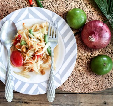 Tabakta Tayland papaya salatası, kakalı papaya salatası, limon, biber, ahşap masada beyaz kasede kırmızı domates.