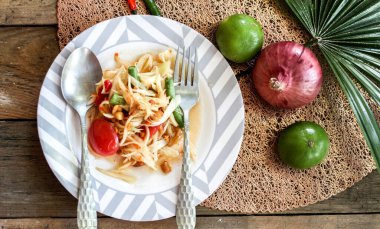 Tabakta Tayland papaya salatası, kakalı papaya salatası, limon, biber, ahşap masada beyaz kasede kırmızı domates.
