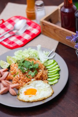 Kızarmış sosis, salatalık, doğranmış sebzeler ile servis edilen Amerikan pilavı kahverengi ahşap bir masada, Tayland soslu..