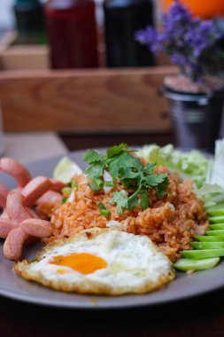 Kızarmış sosis, salatalık, doğranmış sebzeler ile servis edilen Amerikan pilavı kahverengi ahşap bir masada, Tayland soslu..
