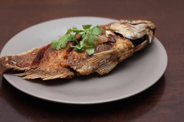 Kızarmış tilapia tam kıvamındaydı. Tayland 'da bir restoranda kahverengi ahşap bir masada gri işler yapmış..