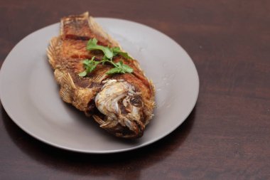 Kızarmış tilapia tam kıvamındaydı. Tayland 'da bir restoranda kahverengi ahşap bir masada gri işler yapmış..