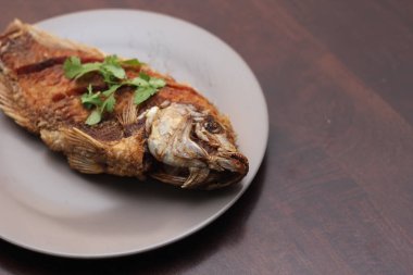 Kızarmış tilapia tam kıvamındaydı. Tayland 'da bir restoranda kahverengi ahşap bir masada gri işler yapmış..
