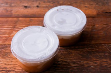 Kahverengi ahşap bir masada plastik bardaklarda hindistancevizi kremalı tatlı pirinç eriştesi..