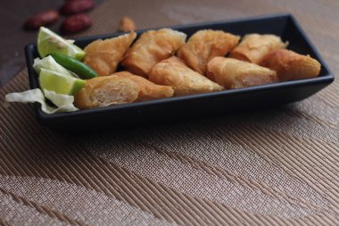 Siyah bir tabakta siyah ahşap bir masada demirhindi sosuyla servis edilen kızarmış börekler.