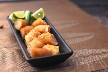 Siyah bir tabakta siyah ahşap bir masada demirhindi sosuyla servis edilen kızarmış börekler.