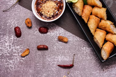 Kızarmış börekler siyah bir tabakta servis edilir masaya demirhindi sosu ile siyah ve altın kaplama ile servis edilir..