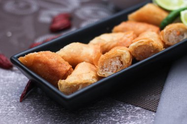 Kızarmış börekler siyah bir tabakta servis edilir masaya demirhindi sosu ile siyah ve altın kaplama ile servis edilir..