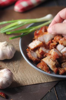 Balık soslu kızarmış domuz eti, siyah ahşap zeminde gri bir tabakta servis edilir..