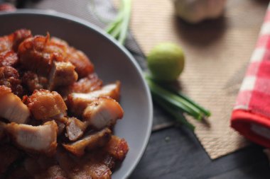 Balık soslu kızarmış domuz eti, siyah ahşap zeminde gri bir tabakta servis edilir..