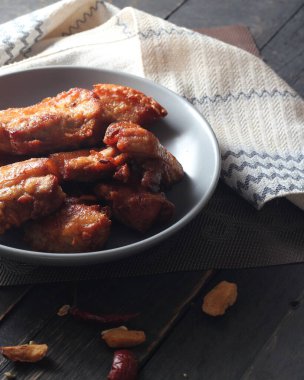 Balık soslu kızarmış domuz eti, siyah ahşap zeminde gri bir tabakta servis edilir..