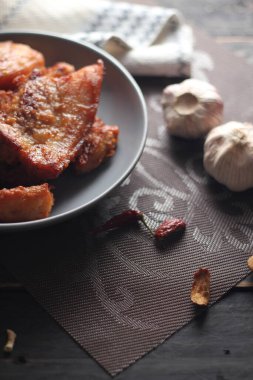 Balık soslu kızarmış domuz eti, siyah ahşap zeminde gri bir tabakta servis edilir..