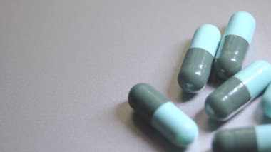 Gri arkaplana yerleştirilmiş mavi-yeşil hap kapsülleri.