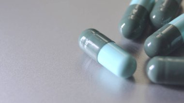Gri arkaplana yerleştirilmiş mavi-yeşil hap kapsülleri.