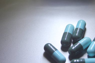 Blue-green pill capsules were placed on a silver table. clipart