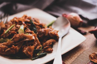 Beyaz tabakta servis edilen siyah soya soslu kızarmış erişteyi karıştır. Siyah tahta masada ya da 