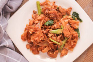 Beyaz tabakta servis edilen Tayland Soya Sosu Kızarmış Eriştesi. Siyah tahta masada ya da 