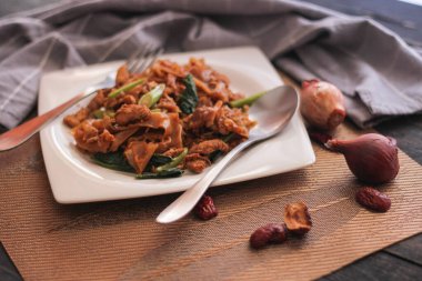 Beyaz tabakta servis edilen siyah soya soslu kızarmış erişteyi karıştır. Siyah tahta masada ya da 