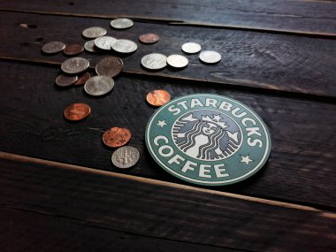Bangkok, Tayland - 23 Haziran 2021: Bardak altlıklarında Starbucks logosu ve siyah ahşap zeminde Amerikan para birimi paraları.