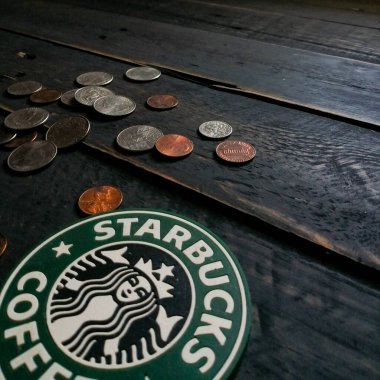 Bangkok, Tayland - 23 Haziran 2021: Bardak altlıklarında Starbucks logosu ve siyah ahşap zeminde Amerikan para birimi paraları.