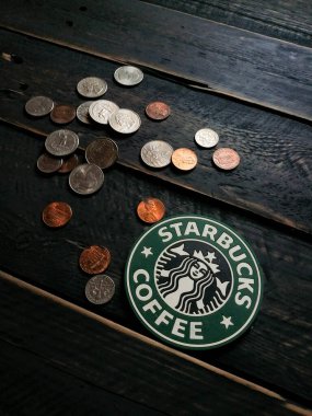 Bangkok, Tayland - 23 Haziran 2021: Bardak altlıklarında Starbucks logosu ve siyah ahşap zeminde Amerikan para birimi paraları.