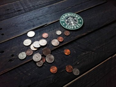 Bangkok, Tayland - 23 Haziran 2021: Bardak altlıklarında Starbucks logosu ve siyah ahşap zeminde Amerikan para birimi paraları.