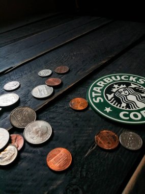 Bangkok, Tayland - 23 Haziran 2021: Bardak altlıklarında Starbucks logosu ve siyah ahşap zeminde Amerikan para birimi paraları.