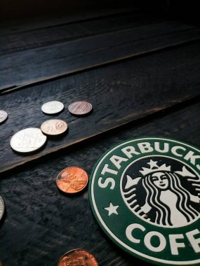 Bangkok, Tayland - 23 Haziran 2021: Bardak altlıklarında Starbucks logosu ve siyah ahşap zeminde Amerikan para birimi paraları.