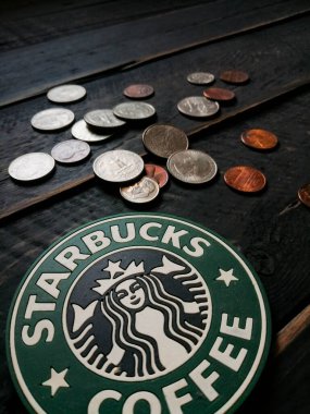 Bangkok, Tayland - 23 Haziran 2021: Bardak altlıklarında Starbucks logosu ve siyah ahşap zeminde Amerikan para birimi paraları.
