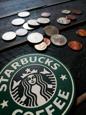 Bangkok, Tayland - 23 Haziran 2021: Bardak altlıklarında Starbucks logosu ve siyah ahşap zeminde Amerikan para birimi paraları.