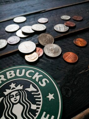 Bangkok, Tayland - 23 Haziran 2021: Bardak altlıklarında Starbucks logosu ve siyah ahşap zeminde Amerikan para birimi paraları.