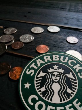 Bangkok, Tayland - 23 Haziran 2021: Bardak altlıklarında Starbucks logosu ve siyah ahşap zeminde Amerikan para birimi paraları.