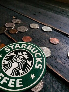 Bangkok, Tayland - 23 Haziran 2021: Bardak altlıklarında Starbucks logosu ve siyah ahşap zeminde Amerikan para birimi paraları.