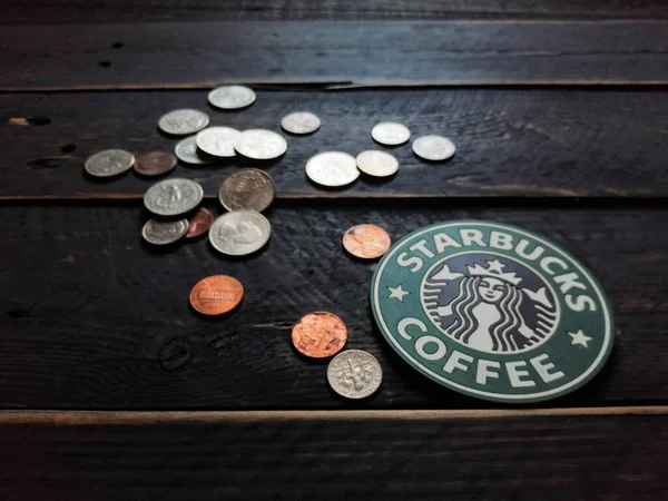 Bangkok, Tayland - 23 Haziran 2021: Bardak altlıklarında Starbucks logosu ve siyah ahşap zeminde Amerikan para birimi paraları.