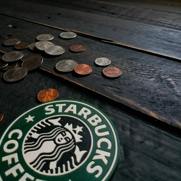 Bangkok, Tayland - 23 Haziran 2021: Bardak altlıklarında Starbucks logosu ve siyah ahşap zeminde Amerikan para birimi paraları.