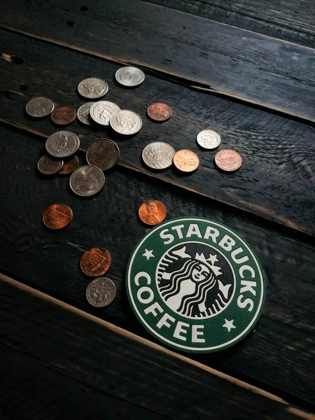 Bangkok, Tayland - 23 Haziran 2021: Bardak altlıklarında Starbucks logosu ve siyah ahşap zeminde Amerikan para birimi paraları.