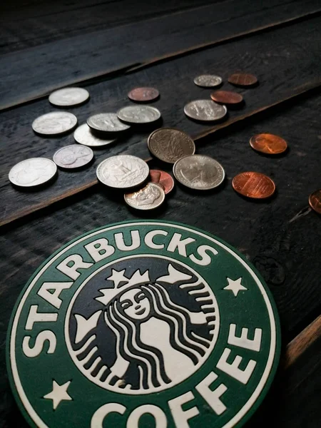 Bangkok, Tayland - 23 Haziran 2021: Bardak altlıklarında Starbucks logosu ve siyah ahşap zeminde Amerikan para birimi paraları.