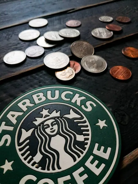 Bangkok, Tayland - 23 Haziran 2021: Bardak altlıklarında Starbucks logosu ve siyah ahşap zeminde Amerikan para birimi paraları.
