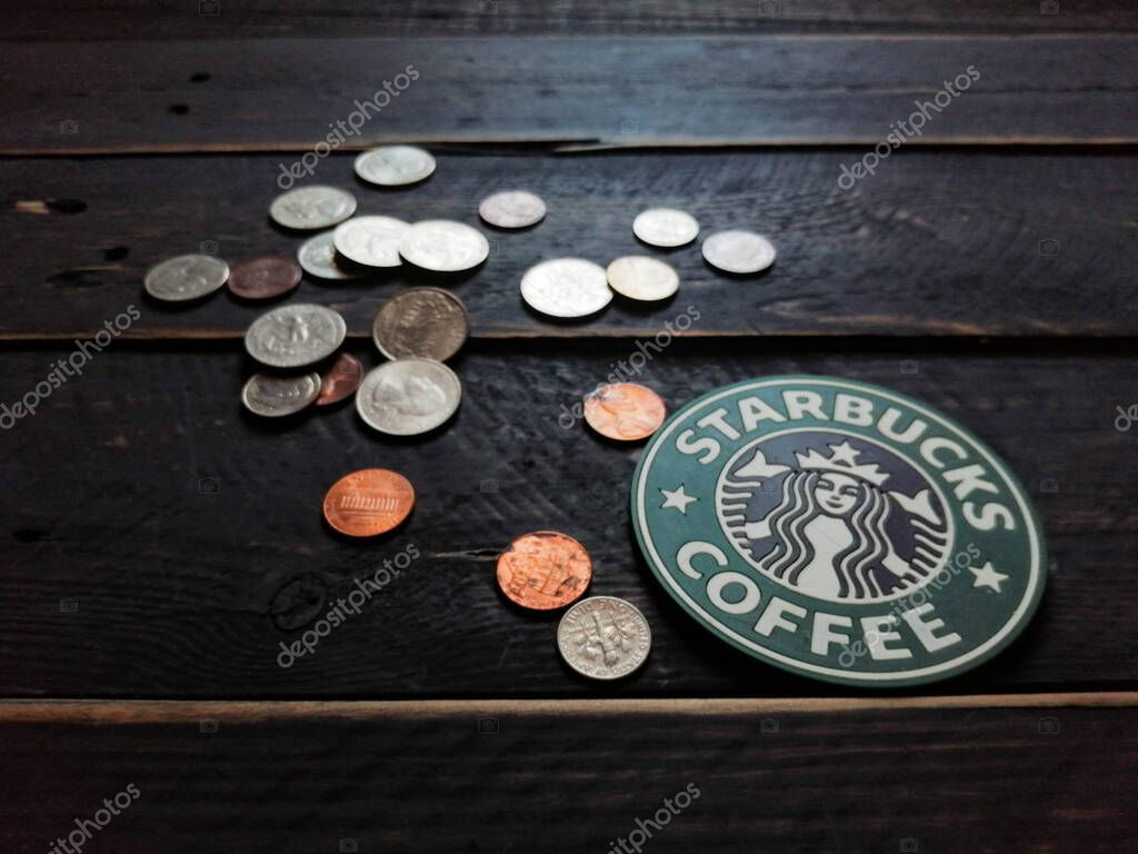Bangkok, Thailand - June,23 2021 : Starbucks logo on coasters and American currency coins on black wooden floor.