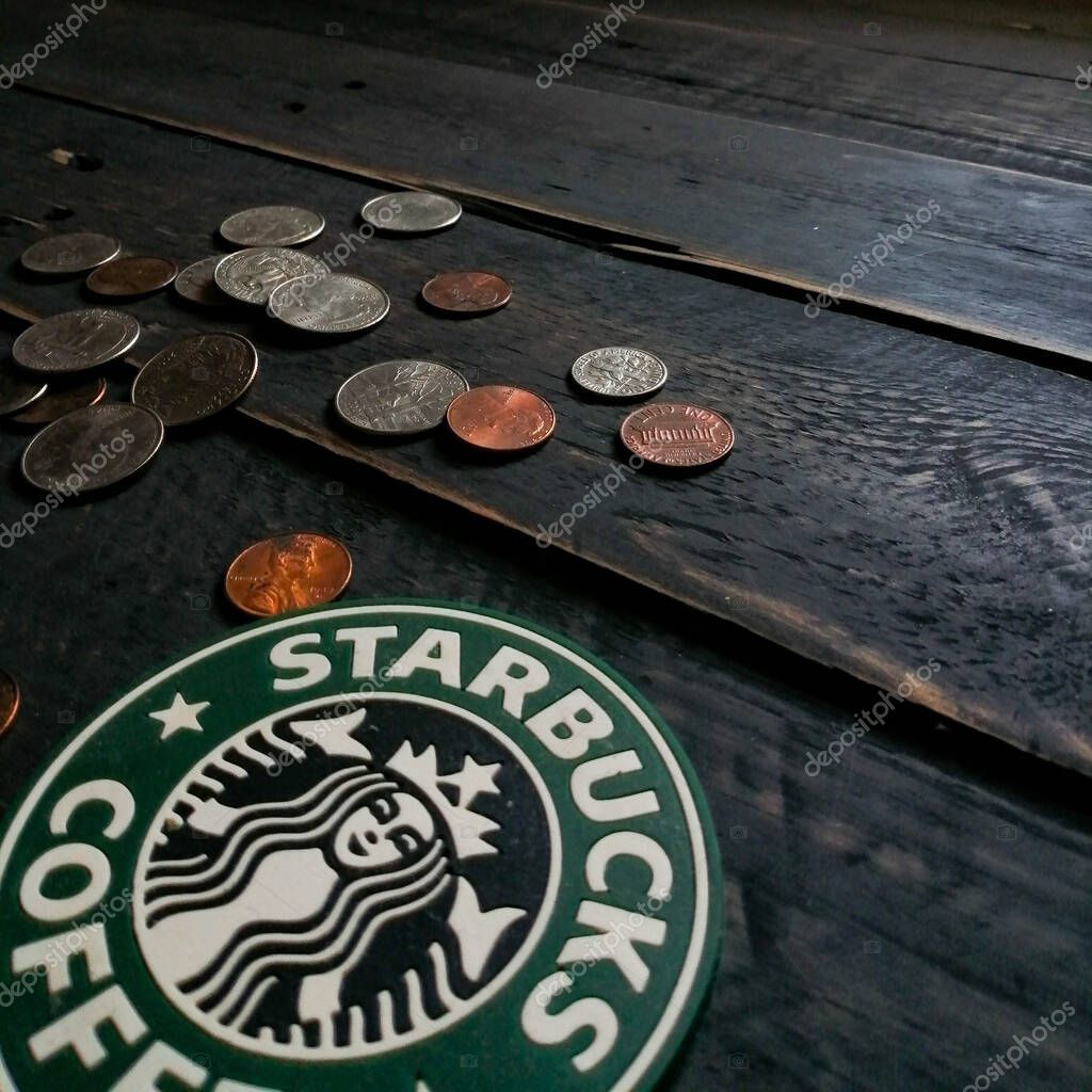 Bangkok, Thailand - June,23 2021 : Starbucks logo on coasters and American currency coins on black wooden floor.