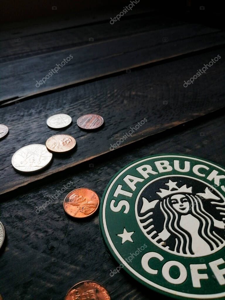 Bangkok, Thailand - June,23 2021 : Starbucks logo on coasters and American currency coins on black wooden floor.