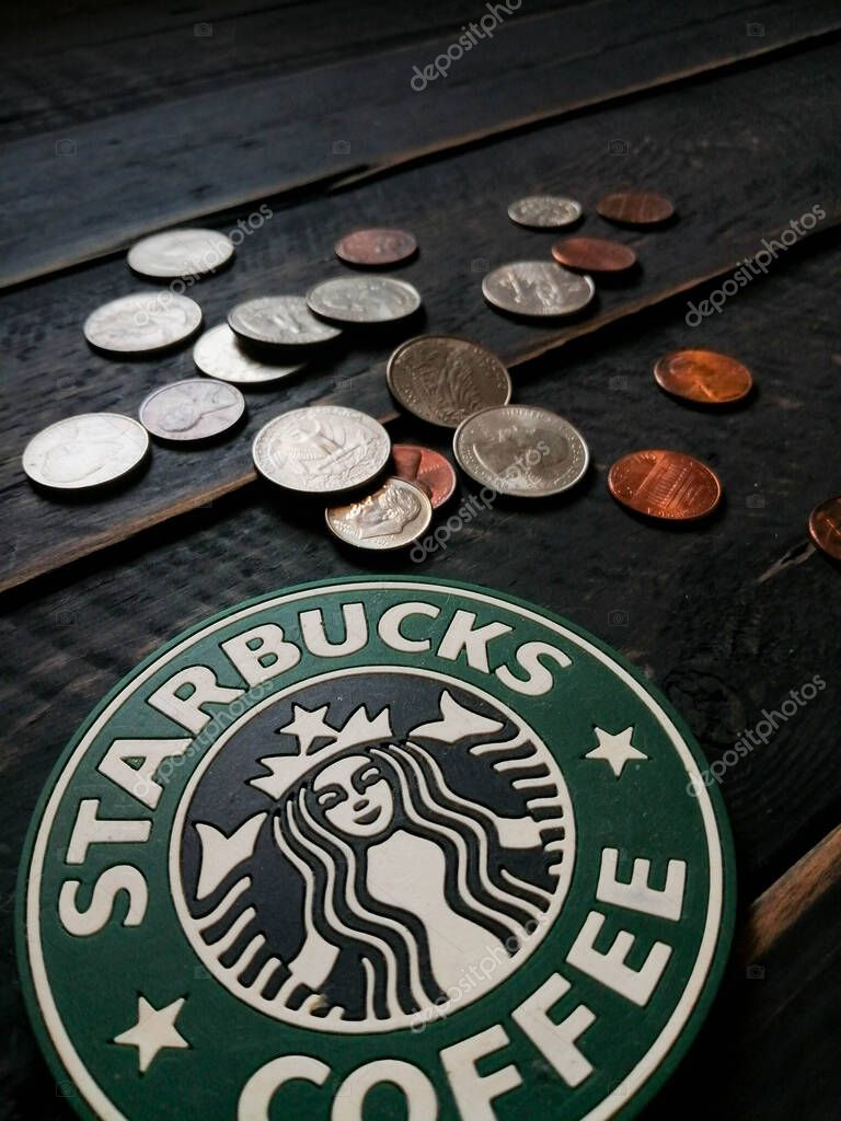 Bangkok, Thailand - June,23 2021 : Starbucks logo on coasters and American currency coins on black wooden floor.