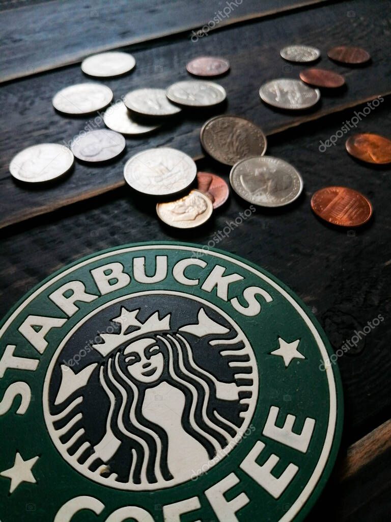 Bangkok, Thailand - June,23 2021 : Starbucks logo on coasters and American currency coins on black wooden floor.