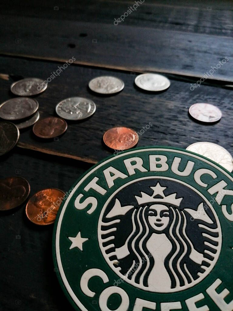Bangkok, Thailand - June,23 2021 : Starbucks logo on coasters and American currency coins on black wooden floor.