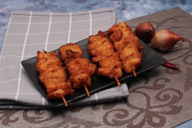 Siyah tabakta servis edilen kızarmış domuz şişleri..