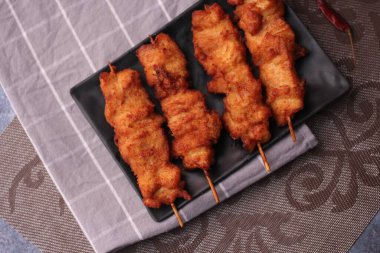 Siyah tabakta servis edilen kızarmış domuz şişleri..