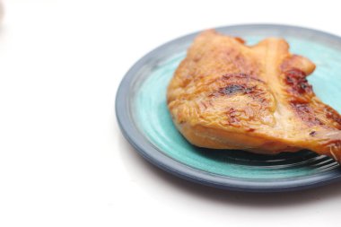 Beyaz bir masada servis edilen yeşil tabakta ızgara tavuk..