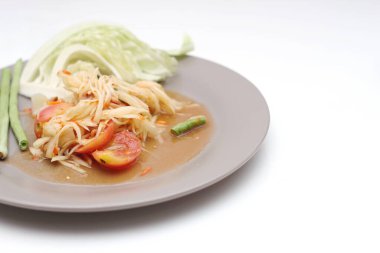 Tabakta Tayland papayası salatası, kakalı papaya salatası, limon, biber, beyaz bir masada gri bir tabakta kırmızı domates..