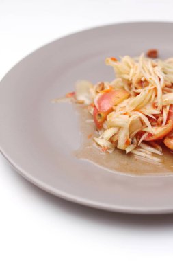 Tabakta Tayland papayası salatası, kakalı papaya salatası, limon, biber, beyaz bir masada gri bir tabakta kırmızı domates..